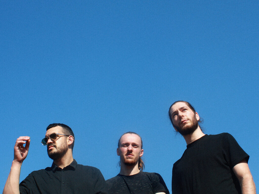 les membres du trio Heavy Crown habillés de noir devant un fond de ciel bleu